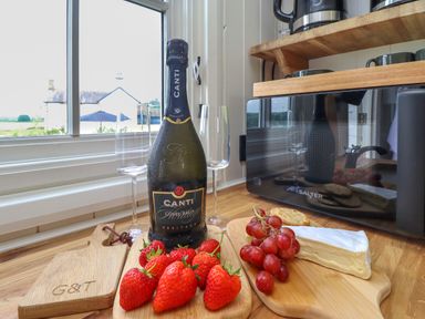 A kitchen counter with a bottle of Canti sparkling wine two wine glasses strawberries grapes cheese crackers and a microwave at La'al Ling in Penrith