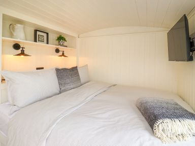 A bedroom with a bed featuring white and grey bedding a blanket a mounted television and a shelf with a pitcher a framed picture and a plant at La'al Ling in Penrith