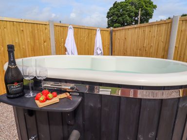 An outdoor hot tub with a bottle of champagne two glasses and strawberries on a small shelf at La'al Ling in Penrith