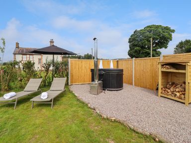 An outdoor area with two lounge chairs, an umbrella, a hot tub, and a wood storage shed at La'al Ling in Penrith