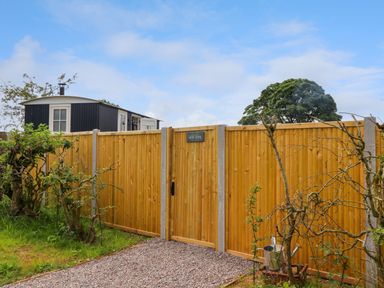 A wooden fence with a gate and a sign that says La'al Ling with a gravel path and a small dark building behind the fence at La'al Ling in Penrith