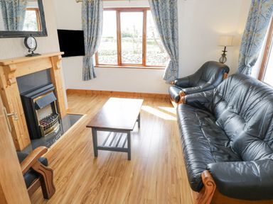 A living room with black leather sofa and armchair a wooden coffee table fireplace and blue floral curtains at Rossaveel Upper in Rossaveel County Galway