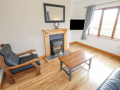 A living room with a wooden coffee table black cushioned wooden armchair fireplace and a window with curtains at Rossaveel Upper in Rossaveel County Galway