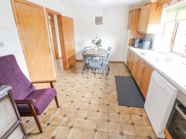 A kitchen with wooden cabinets a dining table with chairs and a dishwasher at Rossaveel Upper in Rossaveel County Galway