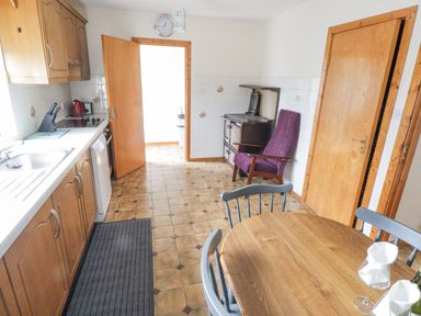 A kitchen with wooden cabinets a dining table and chairs an armchair and an old stove at Rossaveel Upper in Rossaveel County Galway