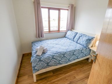 A bedroom with a bed with blue patterned bedding and pillows next to a window with curtains at Rossaveel Upper in Rossaveel County Galway