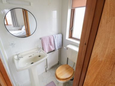 A bathroom with a pedestal sink, a round mirror, a toilet with a wooden seat, two towels hanging on a rack, and a window at Rossaveel Upper in Rossaveel County Galway