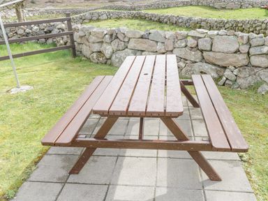 A wooden picnic table on a paved area with grass and stone walls in the background at Rossaveel Upper in Rossaveel County Galway