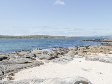 A sandy beach with large rocks and blue water at Rossaveel Upper in Rossaveel County Galway