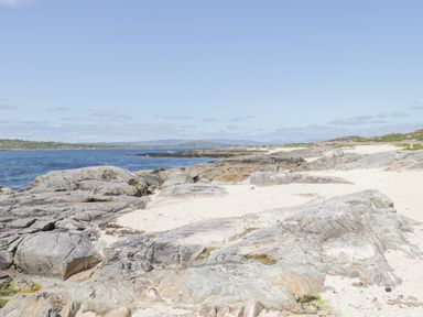 A rocky coastline with sandy patches and a blue sea under a clear sky at Rossaveel Upper in Rossaveel County Galway
