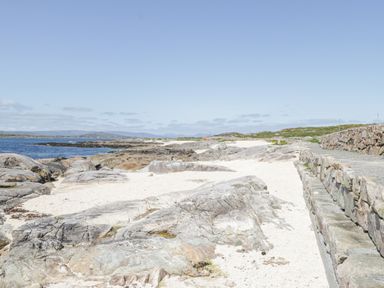 A rocky beach with a stone wall pathway and the sea in the background at Rossaveel Upper in Rossaveel County Galway