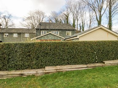 An exterior view of a house with stone walls and windows behind a tall hedge and grass at Ullswater View Apartment in Ullswater