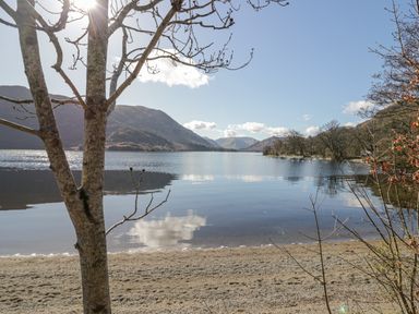 A lakeside view with a sandy shore and bare trees in front of hills at Ullswater View Apartment in Ullswater