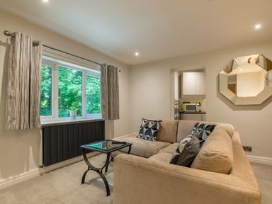 A living room with a beige sofa and glass coffee table near a window with curtains and a wall mirror at Ullswater View Apartment in Ullswater