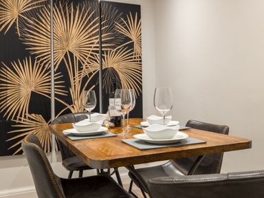 A dining table set with plates bowls wine glasses and a bottle of wine with black chairs and decorative wall art at Ullswater View Apartment in Ullswater