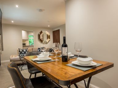 A dining table set with plates wine glasses and a bottle in a room with a sofa and a wall mirror at Ullswater View Apartment in Ullswater