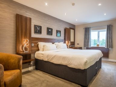 A bedroom with a large bed two bedside lamps a chair and a window with curtains at Ullswater View Apartment Ullswater