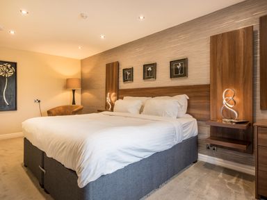 A bedroom with a large bed white linens nightstands with lamps a chair and framed pictures on the wall at Ullswater View Apartment in Ullswater