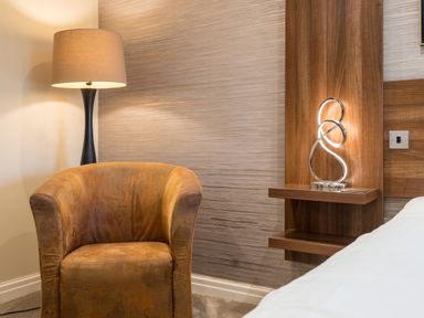A brown armchair next to a floor lamp and wooden wall shelf with a modern decorative light in a bedroom at Ullswater View Apartment Ullswater