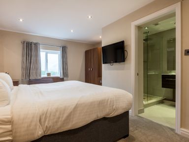 A bedroom with a bed television wardrobe window and an ensuite bathroom at Ullswater View Apartment in Ullswater