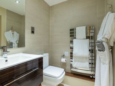 A bathroom with a sink, toilet, towel rack with towels, and a bathrobe hanging on the wall at Ullswater View Apartment in Ullswater