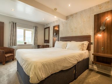 A bedroom with a large bed white bedding a brown armchair a window with curtains and wall lights at Ullswater View Apartment Ullswater