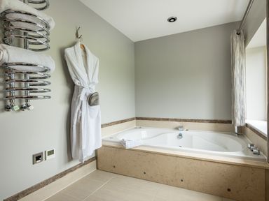 A bathroom with a bathtub a bathrobe hanging on the wall and a heated towel rail at Ullswater View Apartment in Ullswater