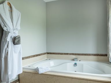 A bathroom with a white bathtub a folded towel on the bathtub edge and a white bathrobe hanging on the wall at Ullswater View Apartment in Ullswater