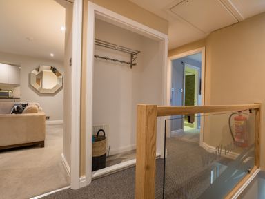 A hallway with an open closet and a basket near a living room with a beige sofa and mirror at Ullswater View Apartment in Ullswater