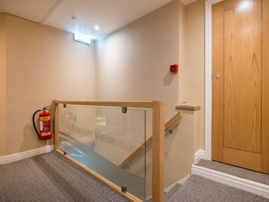 A stairwell with glass and wood railing a fire extinguisher and a closed wooden door at Ullswater View Apartment in Ullswater
