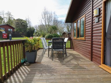 An outdoor wooden deck with a table and chairs next to a cabin at 3 The Glade in St Minver Rock