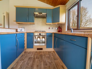 A kitchen with blue cabinets wood countertop gas stove oven toaster and a window showing trees at 3 The Glade in St Minver Rock