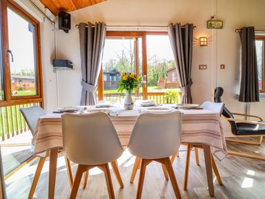 A dining table with plates and a vase of flowers near windows with curtains and a chair at 3 The Glade in St Minver Rock