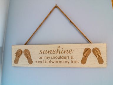 A wooden hanging sign with flip flop decorations and the text sunshine on my shoulders and sand between my toes at 3 The Glade in St Minver Rock