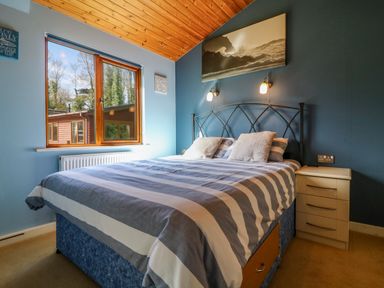 A bedroom with a double bed striped bedding bedside table window and wooden ceiling at 3 The Glade in St Minver Rock