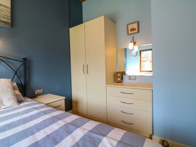 A bedroom with a bed striped bedspread a bedside table wardrobe and dresser with mirror at 3 The Glade in St Minver Rock