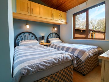 A bedroom with two single beds and a window showing trees and a wooden building at 3 The Glade in St Minver Rock