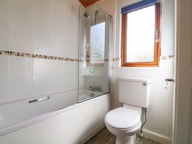 A bathroom with a bathtub shower combination a toilet and a window at 3 The Glade in St Minver Rock