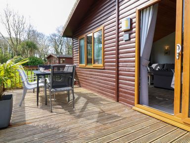 A wooden deck with outdoor table and chairs next to a cabin with an open door showing a living room at 3 The Glade in St Minver Rock