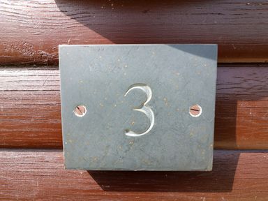 A metal plate with number 3 attached to a wooden surface at 3 The Glade in St Minver Rock