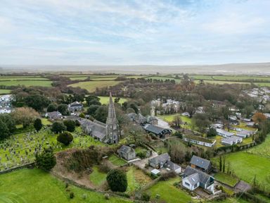 An aerial view of a church with a tall steeple surrounded by gravestones houses and mobile homes in a rural area at 3 The Glade in St Minver Rock
