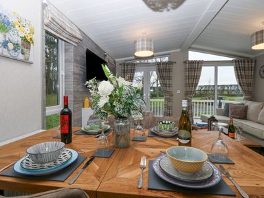 A dining table set with plates bowls wine glasses and bottles in a living area with sofas windows and curtains at Wurzburc in Swaffham