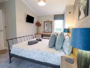 A bedroom with a bed a television on the wall a desk with a mirror and a lamp at Wurzburc in Swaffham