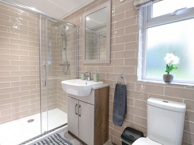 A bathroom with a shower enclosure sink with cabinet mirror toilet and a window with a flower pot at Wurzburc in Swaffham
