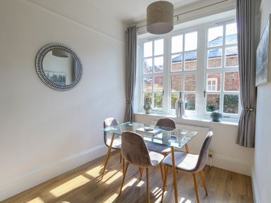 A dining area with a glass table and four chairs near windows with curtains and decorative items at Splash in Weymouth