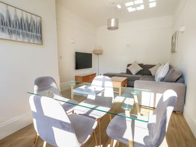 A living room with a gray sofa a wooden coffee table and a glass dining table with four chairs at Splash in Weymouth