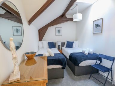 A bedroom with two single beds a bedside table a lamp a chair a wooden dresser with a bowl and a sculpture and two framed pictures at Splash Weymouth