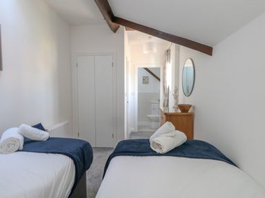 A bedroom with two single beds with blue throws and rolled towels on each bed a wooden dresser with a bowl and statue and an oval mirror on the wall at Splash in Weymouth