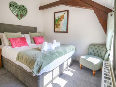 A bedroom with a bed with green and pink pillows a chair a window and framed wall art at Splash in Weymouth