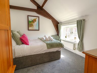 A bedroom with a bed green and pink pillows wooden wardrobe window with green curtains and painting on wall at Splash in Weymouth